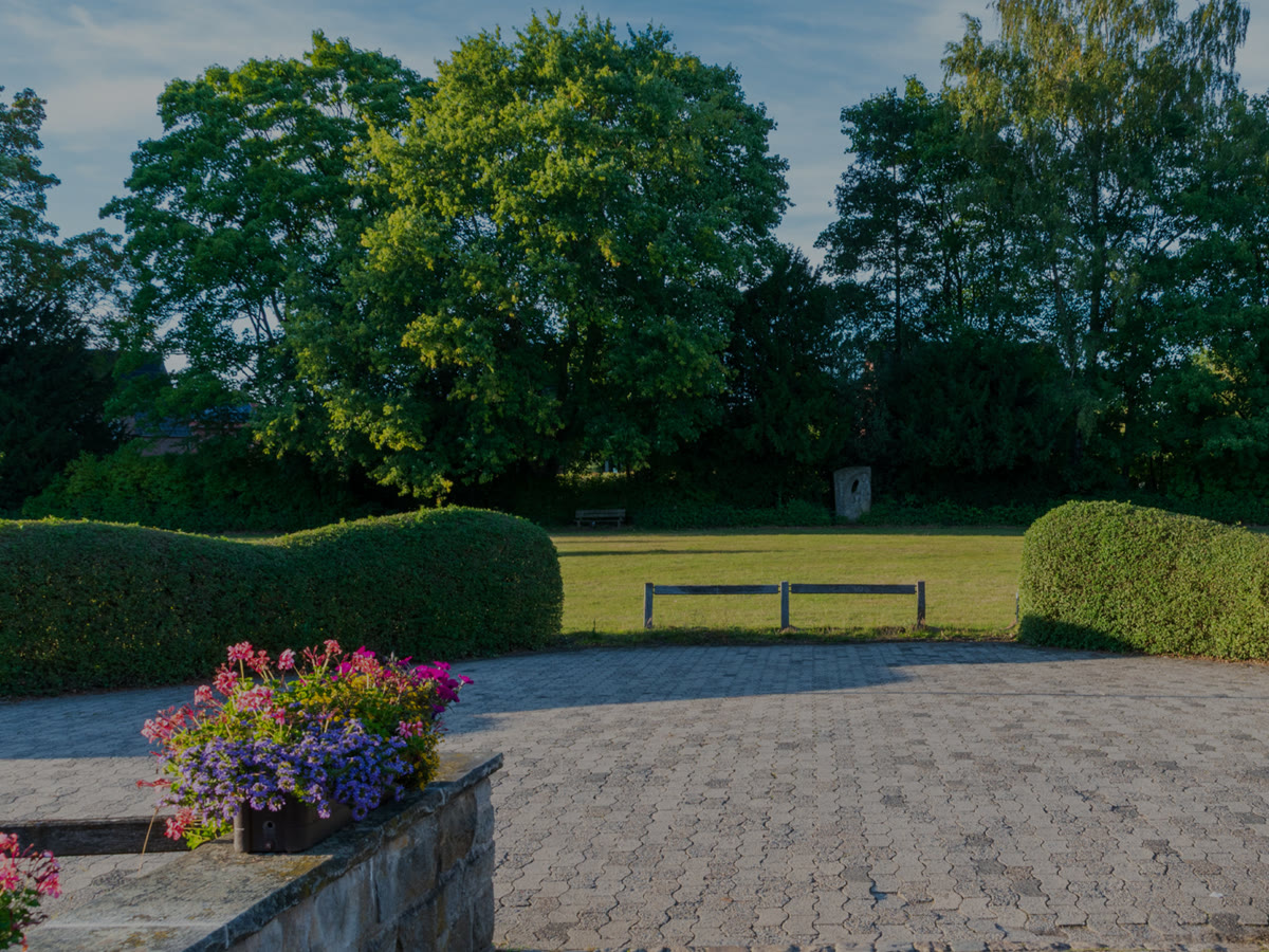 A paver terrace with trimmed hedges, planters and a lawn beyond