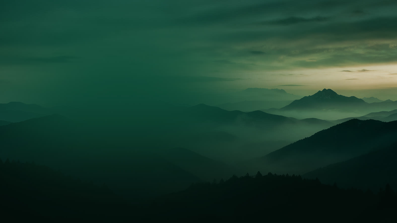 Misty green mountain ridges under a dark sky at dusk