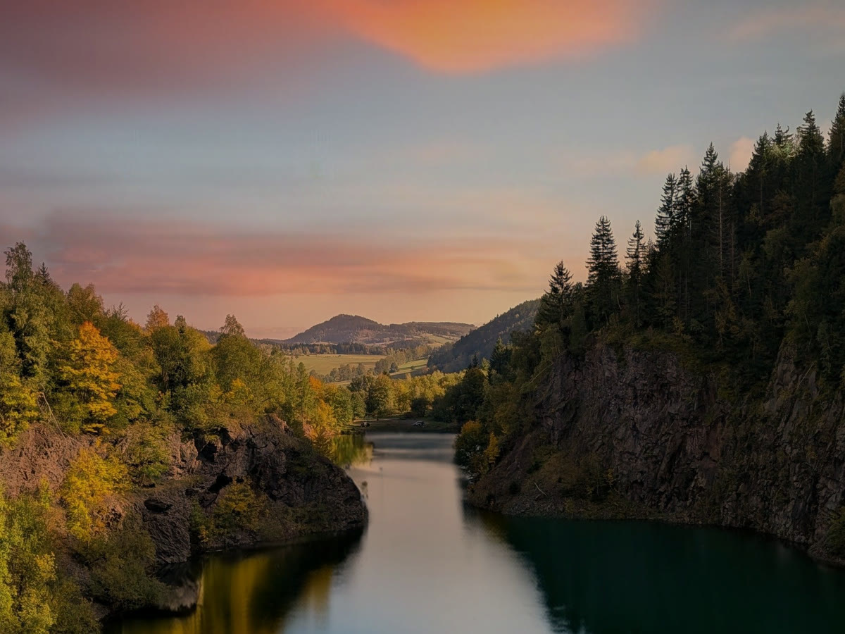 A forest lake between wooded cliffs under a pink sunset sky