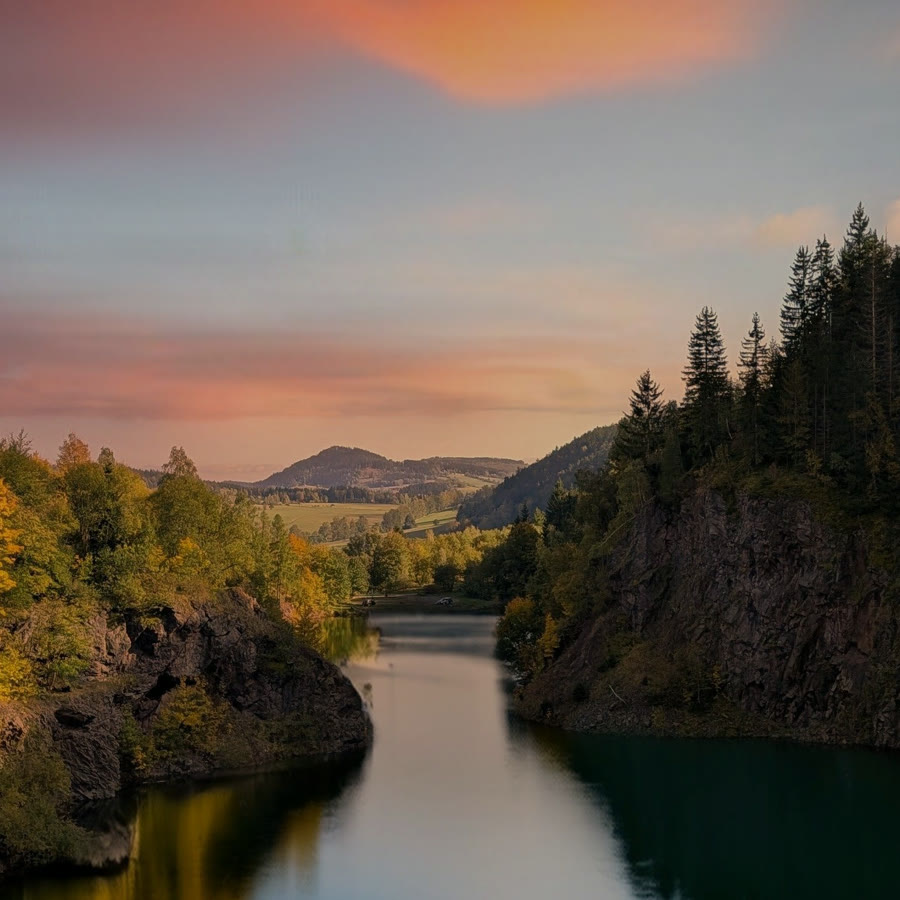 A forest lake between wooded cliffs under a pink sunset sky
