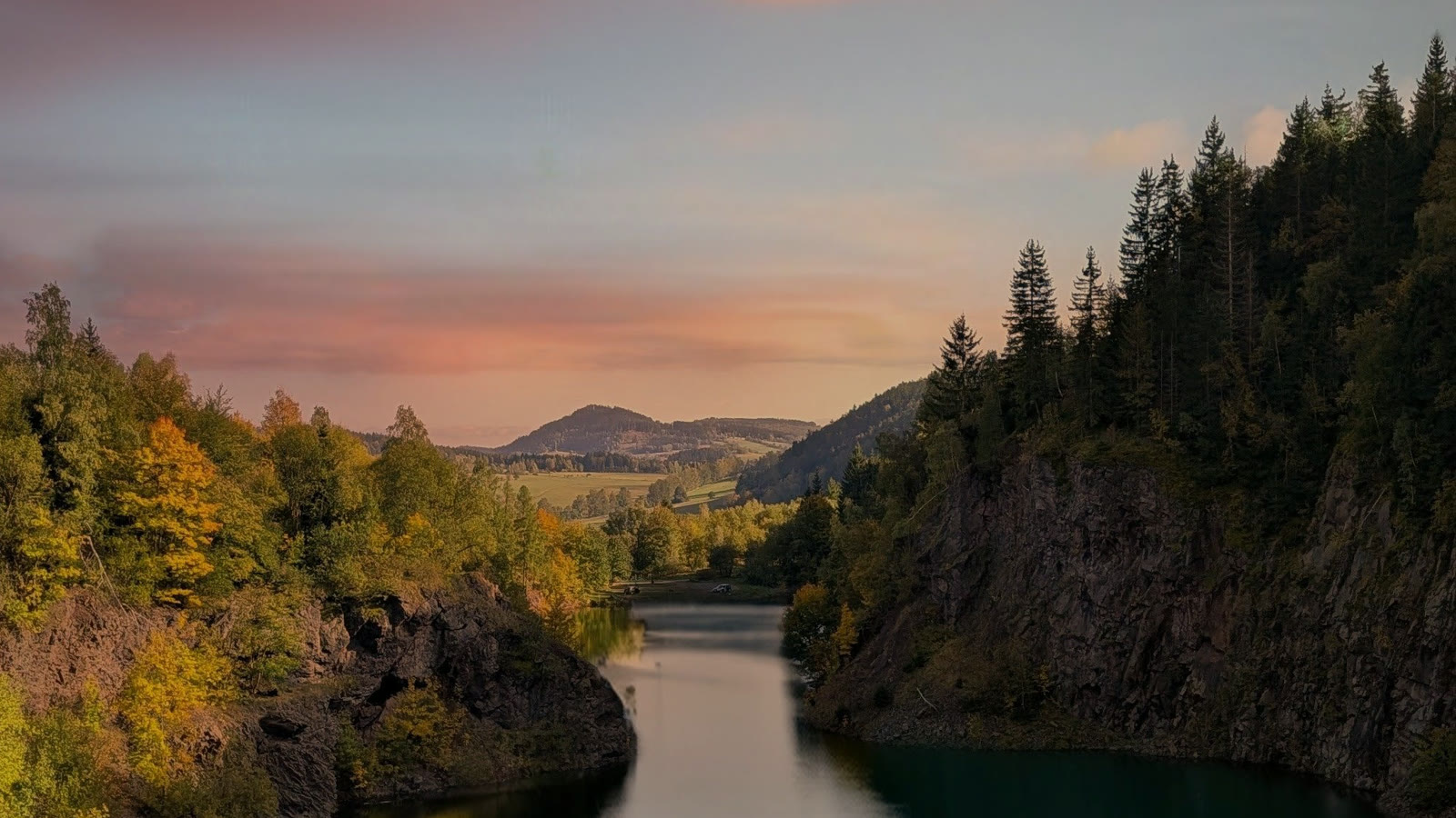A forest lake between wooded cliffs under a pink sunset sky